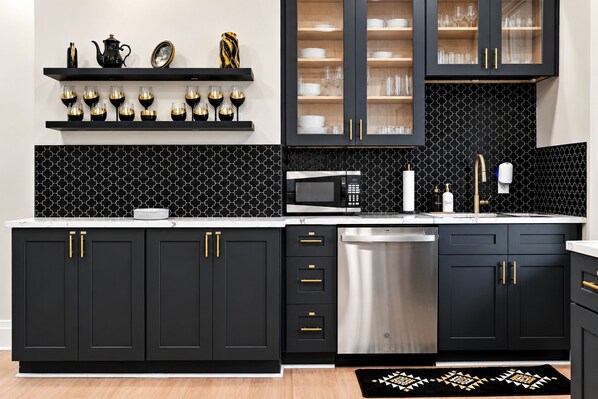 A modern kitchen with black cabinets, gold handles, a stainless steel dishwasher, and a microwave.