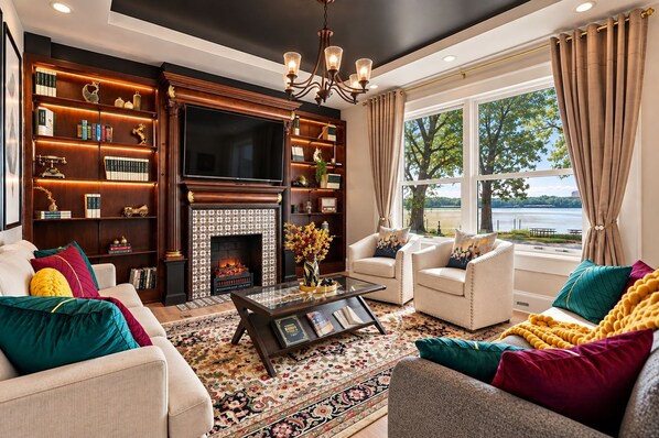 A living room with a fireplace, bookshelves, a coffee table, and a view of a lake.