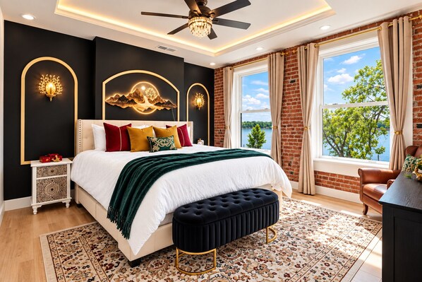 A bedroom with a large bed, a ceiling fan, a view of the outdoors, and a nightstand with decorative items.