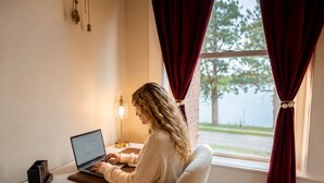 A person working at a desk with a laptop, a lamp, and a window with curtains.