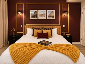 Habitación de hotel con una cama grande, cabecera, dos mesitas de noche, un libro y cuadros en la pared.