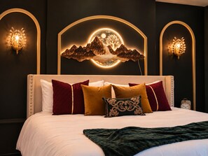 A bedroom with a large bed, multiple pillows, a decorative wall piece, and wall sconces.