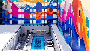 Un área de piscina en la azotea con un cartel que dice 'RESET', rodeada de edificios coloridos con patrones geométricos.