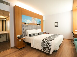 Een hotelkamer met een bed, nachtkastje, bureau, spiegel en een schilderij aan de muur.