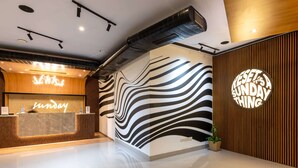 Zona de recepción de hotel con diseño moderno, que incluye un mostrador de recepción, una pared con estampado de rayas de cebra y un letrero circular que dice 'RESEAT SUNDAY THING'.