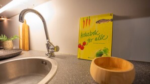 Un évier de cuisine, un saladier en bois et un livre de cuisine intitulé « Kokke for alle » sont posés sur un plan de travail.