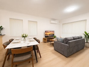 A modern living room with a dining area, grey sofa, and a TV on a stand. - 2BR Apartment Central Rail Station CBD Free Parking (Chippendale)