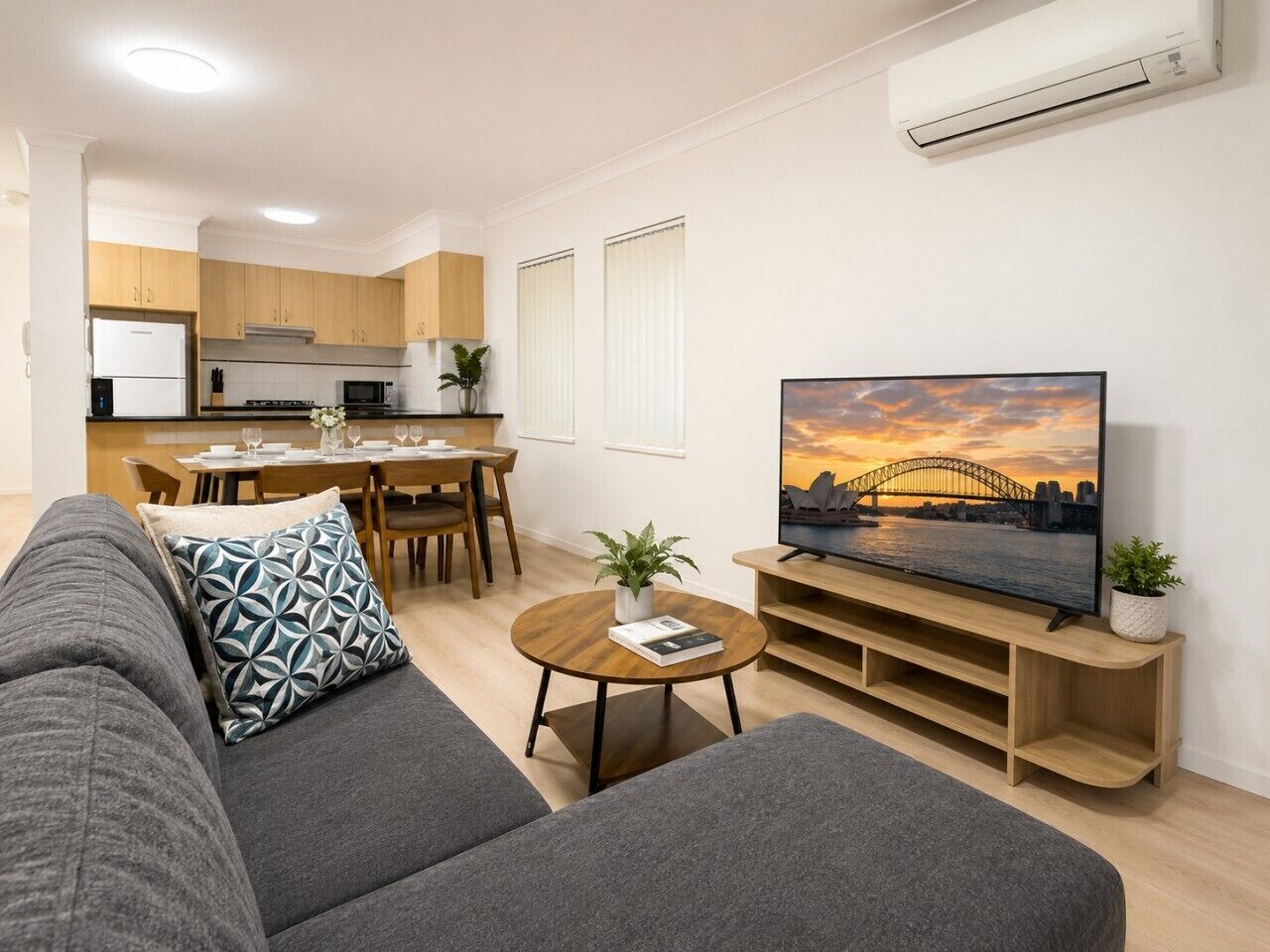 A modern living room with a sofa, a coffee table, a TV, and a dining area in the background.