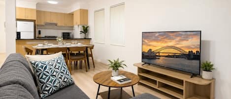 A modern living room with a sofa, a coffee table, a TV, and a dining area in the background.