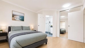Una camera da letto con un letto, comodini, un tavolino da notte, un quadro e una porta scorrevole che dà su un'altra stanza.