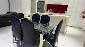 Uma cozinha moderna com armários brancos, painel de parede vermelho e uma mesa de jantar de vidro com quatro cadeiras.