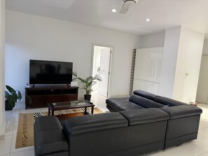 Ein modernes Wohnzimmer mit einem großen schwarzen Ledersofa, einem Flachbildfernseher, einer Holzunterhaltungseinheit und einer Topfpflanze.