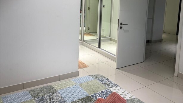 Quarto com uma cama, uma porta de vidro que dá para um banheiro e um corredor.