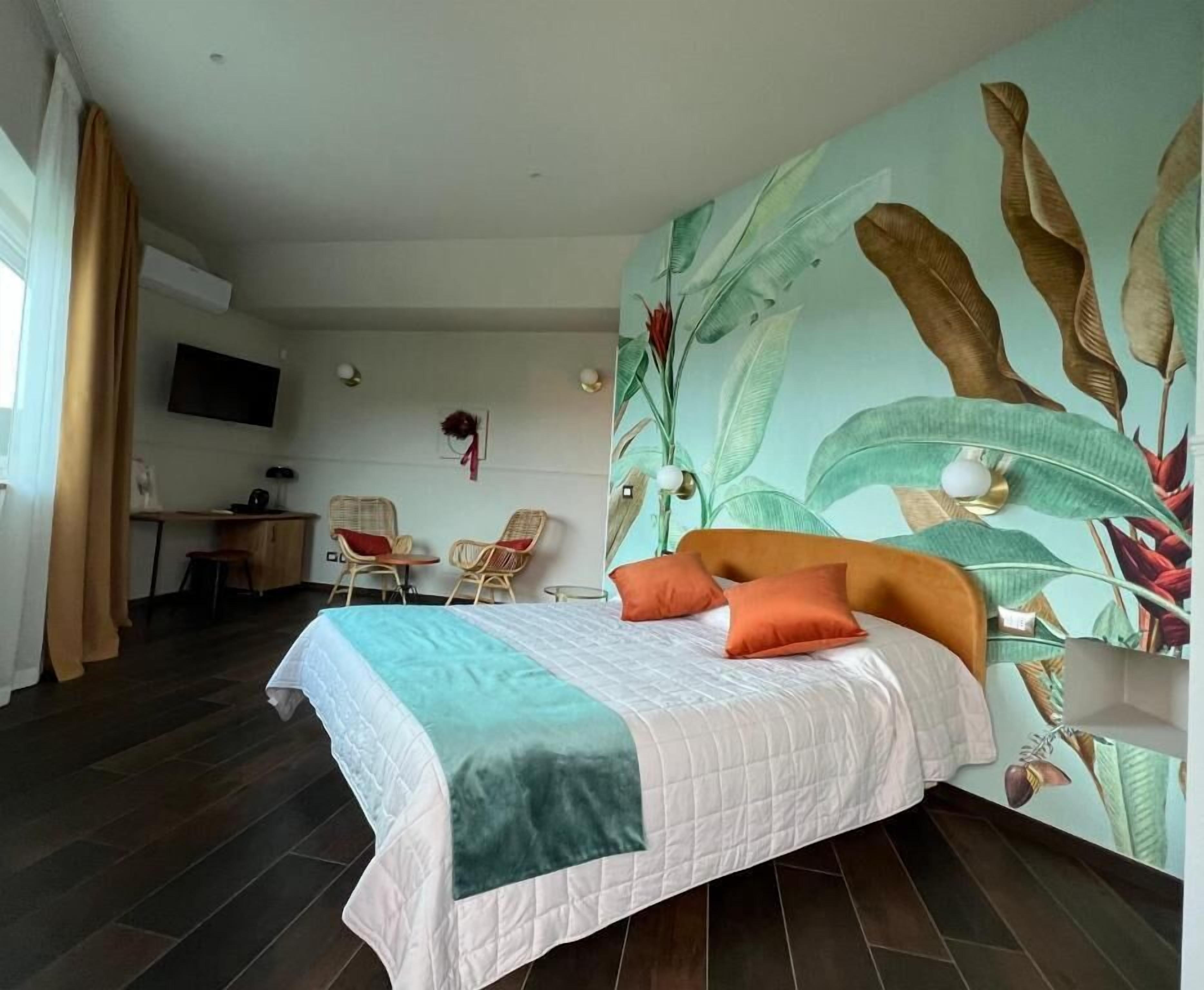 A hotel room with a bed, a desk, chairs, and a large wall mural.