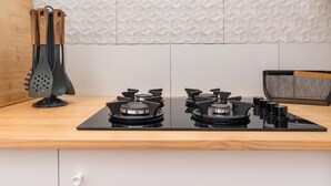 Une cuisine avec une plaque de cuisson noire, un plan de travail en bois et un pare-feu orné d’un motif géométrique.