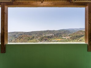 Une vue à travers une fenêtre à cadre en bois, donnant sur un paysage vallonné parsemé de bâtiments.