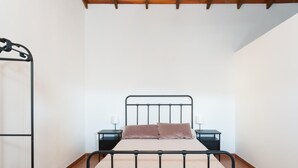 Un lit simple avec un cadre en métal, deux tables de chevet avec des lampes et une étagère fixée au mur.