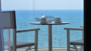 A balcony with a table and two chairs, overlooking the sea with a ship in the distance.