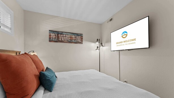Ein Hotelzimmer mit Bett, Kissen, einem Wand-Fernseher und einem gerahmten Bild.