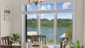 Ein Essbereich mit einem Tisch für vier Personen, große Fenster mit Blick auf einen See und umliegendes Grün.