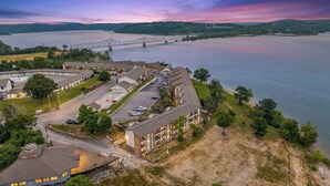 A hotel with multiple buildings, a parking lot, and a view of a river with a bridge in the background.