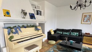 Una sala de estar con un piano, un sofá negro, una mesa de centro y una alfombra estampada.