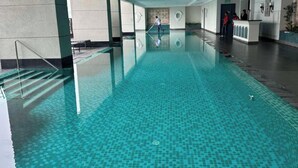 En stor indendørs swimmingpool med klart blåt vand, en reception og en person, der rengør poolen.