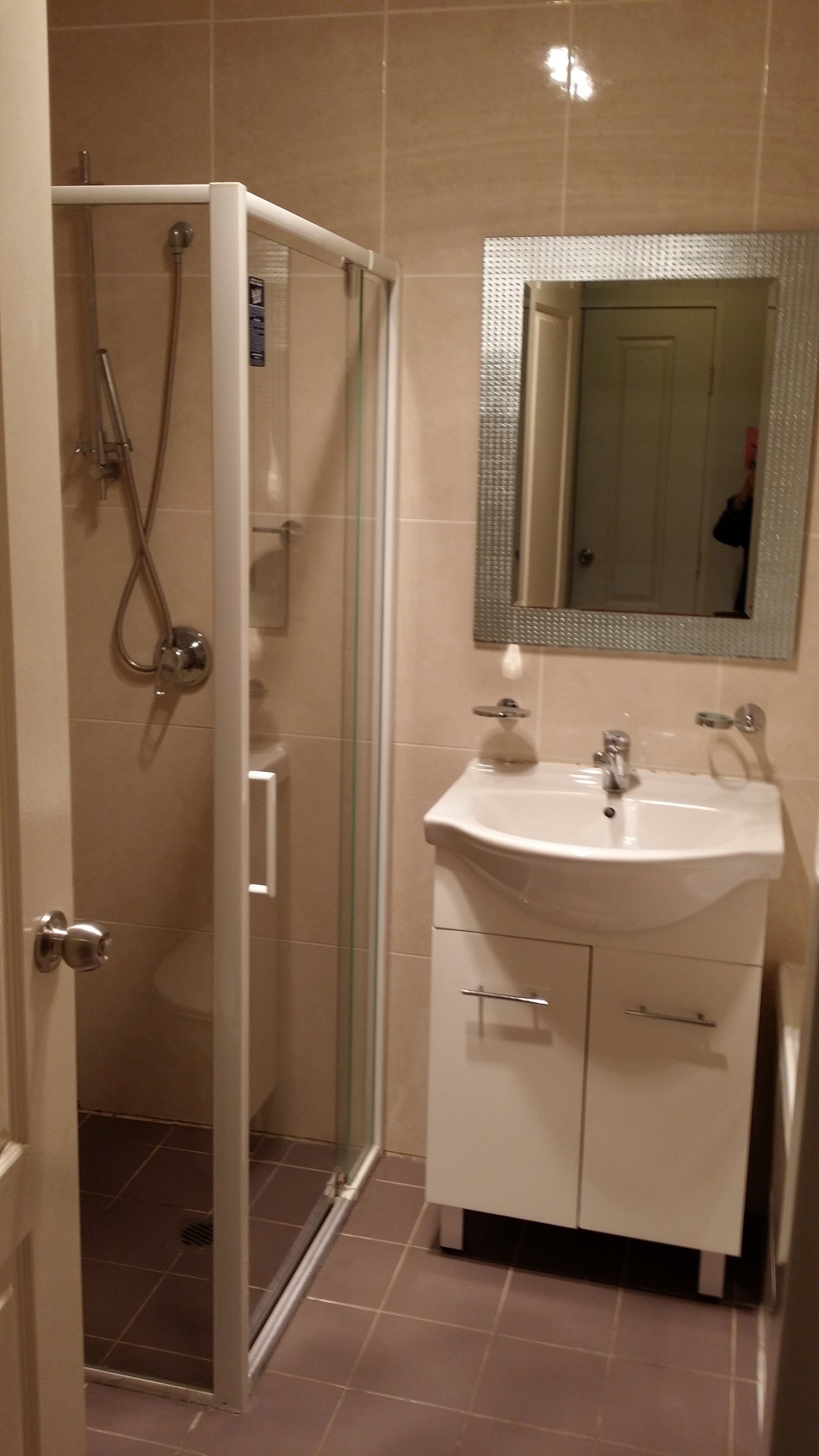 Een badkamer met een douchecabine van glas, een wastafel en een spiegel.