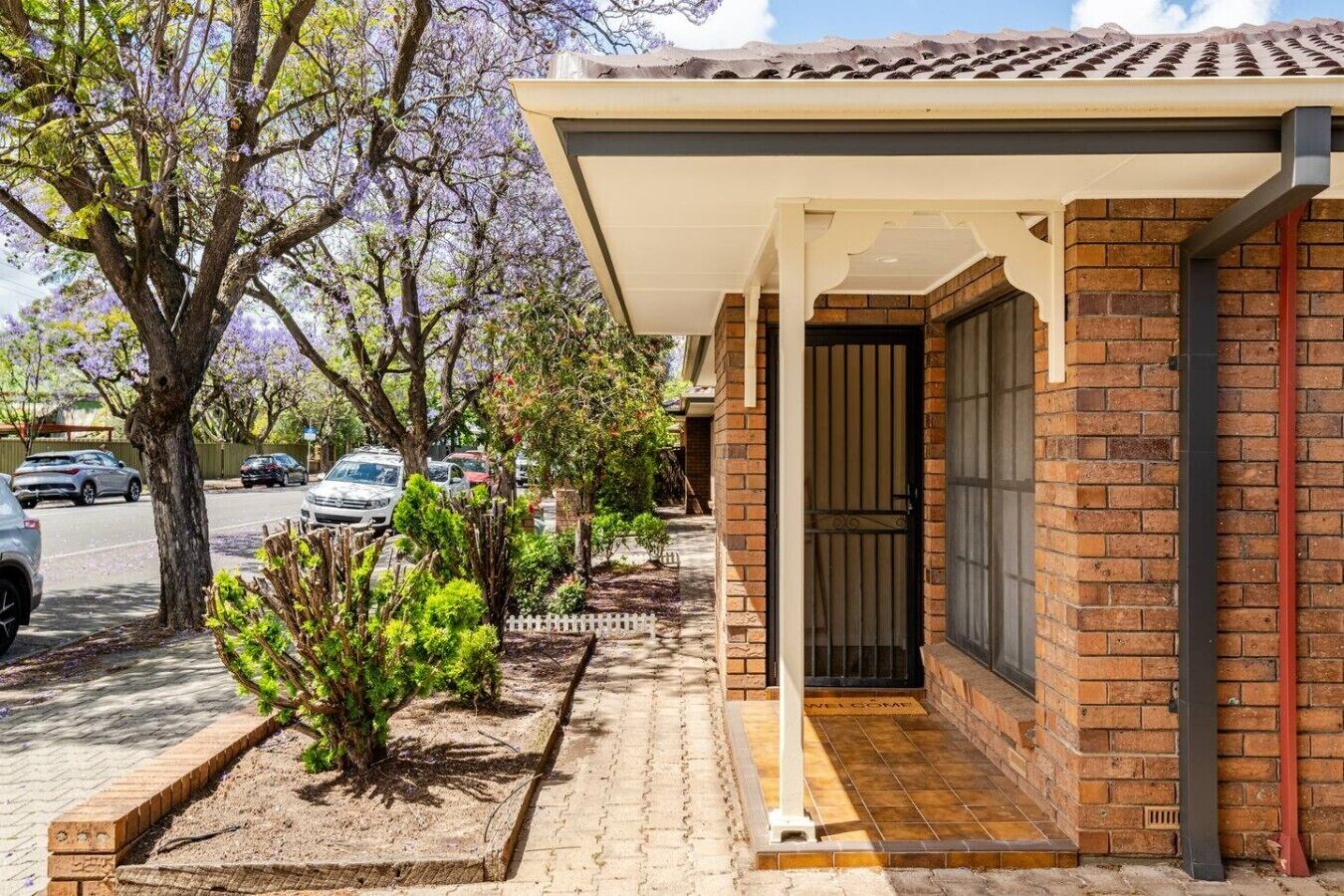 A residential property with a brick exterior, a covered porch, and a small garden area with shrubs.