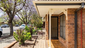 A residential property with a brick exterior, a covered porch, and a small garden area with shrubs.