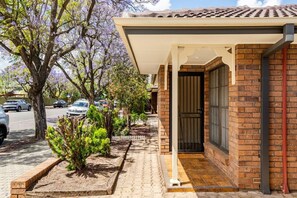 A residential property with a brick exterior, a covered porch, and a small garden area with shrubs. - Spacious Unley Home | Fast WiFi & Free Parking (Unley)