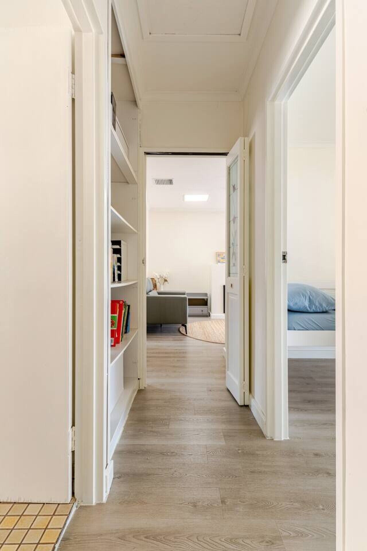A narrow hallway with a bookshelf, a desk, and a bed in the distance.