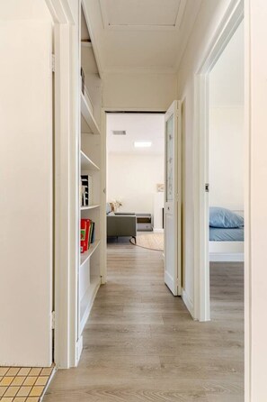 A narrow hallway with a bookshelf, a desk, and a bed in the distance. - Spacious Unley Home | Fast WiFi & Free Parking (Unley)