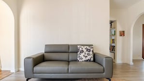 A grey sofa with a floral pillow in a room with white walls and a wooden floor.