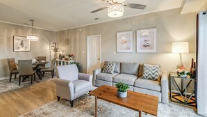 A living room with a ceiling fan, a dining area with chairs and a table, and a sofa with decorative pillows. - The Breeze at Lewes Condo w/ Pool | Bike to Beach! (Lewes)