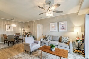 Ein Wohnzimmer mit Deckenventilator, eine Essecke mit Stühlen und einem Tisch sowie ein Sofa mit Zierkissen.