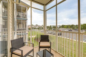 A balcony with two wicker chairs and a small table, overlooking a parking lot and buildings. - The Breeze at Lewes Condo w/ Pool | Bike to Beach! (Lewes)
