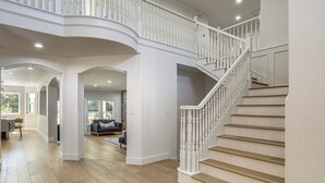 Un interior espacioso con una imponente escalera, pisos de madera y una sala de estar con un sofá y sillones.