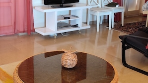 A living room with a round glass table, a television on a white stand, a patterned rug, and a door in the background. - Stunning villa with ocean views, 100 meters from the beach (Roquebrune-sur-Argens)