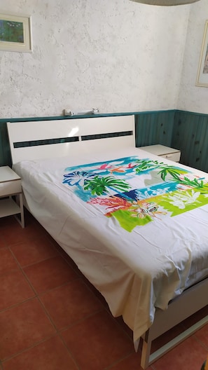 Una cama con una colcha floral de colores, un cabecero blanco y una mesita de noche con una lámpara.