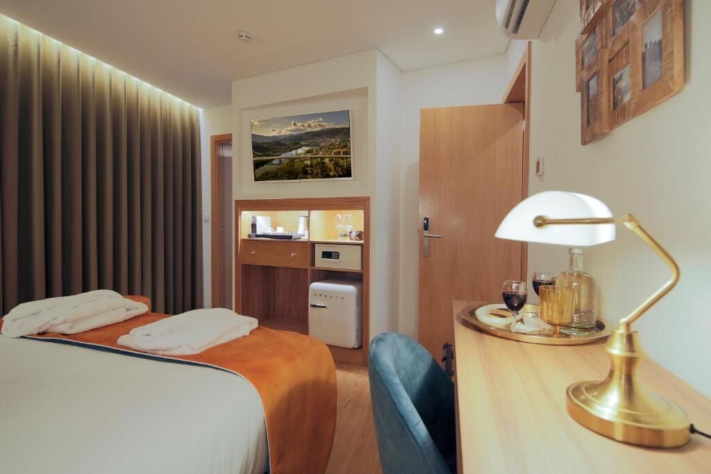 A hotel room with a bed, a desk with a lamp, a small kitchenette, and a wall-mounted TV.