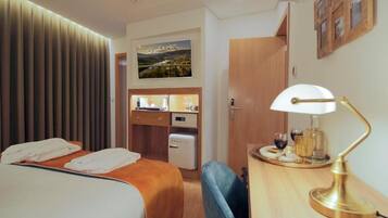 A hotel room with a bed, a desk with a lamp, a small kitchenette, and a wall-mounted TV.
