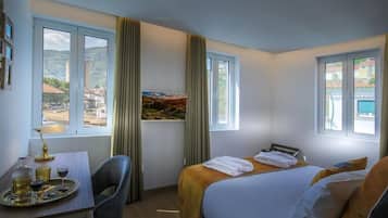 A hotel room with a bed, a table with a tray of glasses, a chair, and a window with curtains.