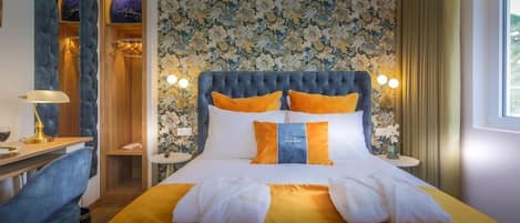A hotel room with a large bed, a desk, and a chair. There is a mirror and a window with curtains.