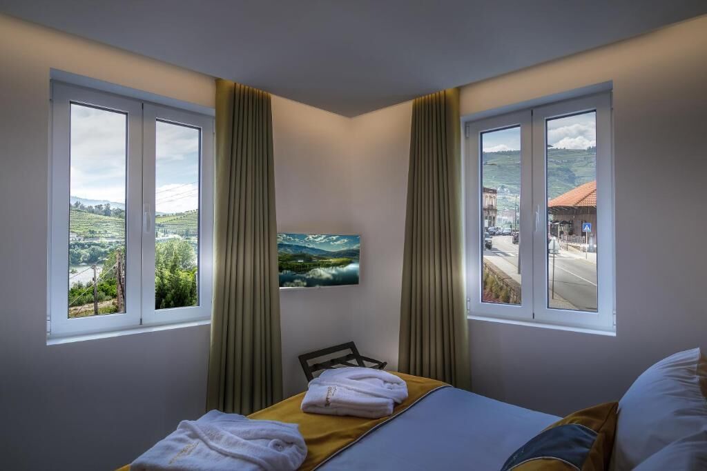Habitación de hotel con cama, una silla y dos ventanas con cortinas.