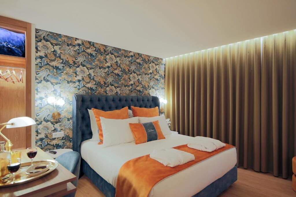 Quarto de hotel com uma cama grande, uma mesa de cabeceira com abajur e parede com padrão floral.