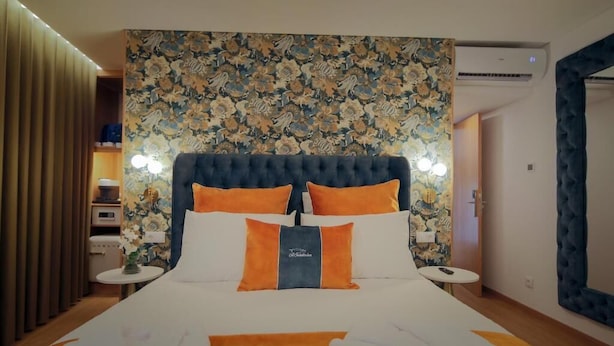 Habitación de hotel con una cama grande, cabecera con estampado floral y una mesita de noche con lámpara.