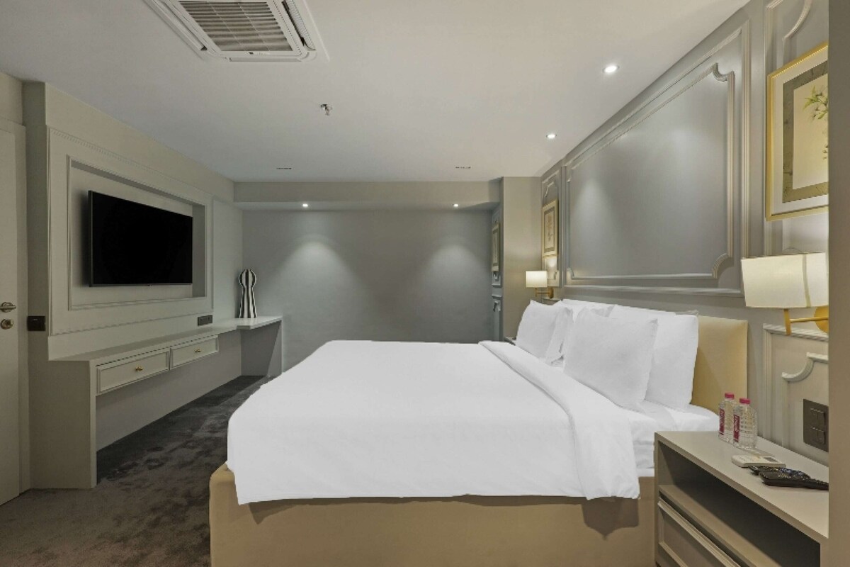 Hotelkamer met groot bed, flatscreen televisie, bureau met lamp en spiegel.