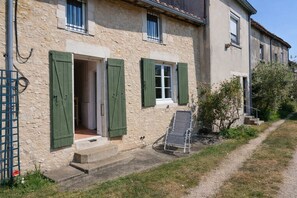 A stone building with green shutters, a door, and a small outdoor seating area. - Gite des Anglais proche de Poitiers (Marnay)