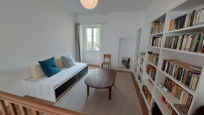 A room with a sofa, a round table, a bookshelf, and a window. - Gite des Anglais proche de Poitiers (Marnay)